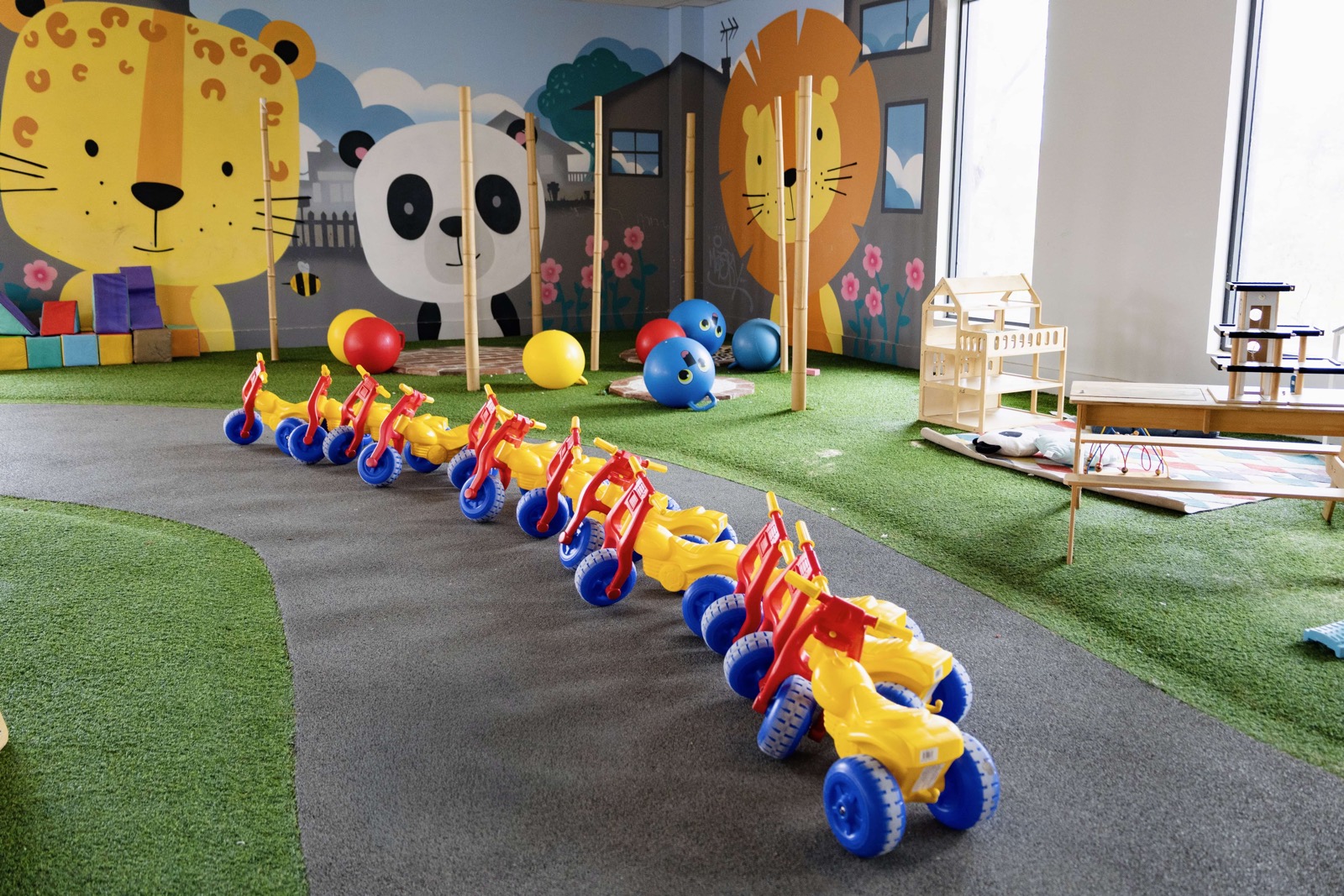 The jungle play room at Cubs Corner, with a lion and tiger mural, artificial grass and a row of trikes